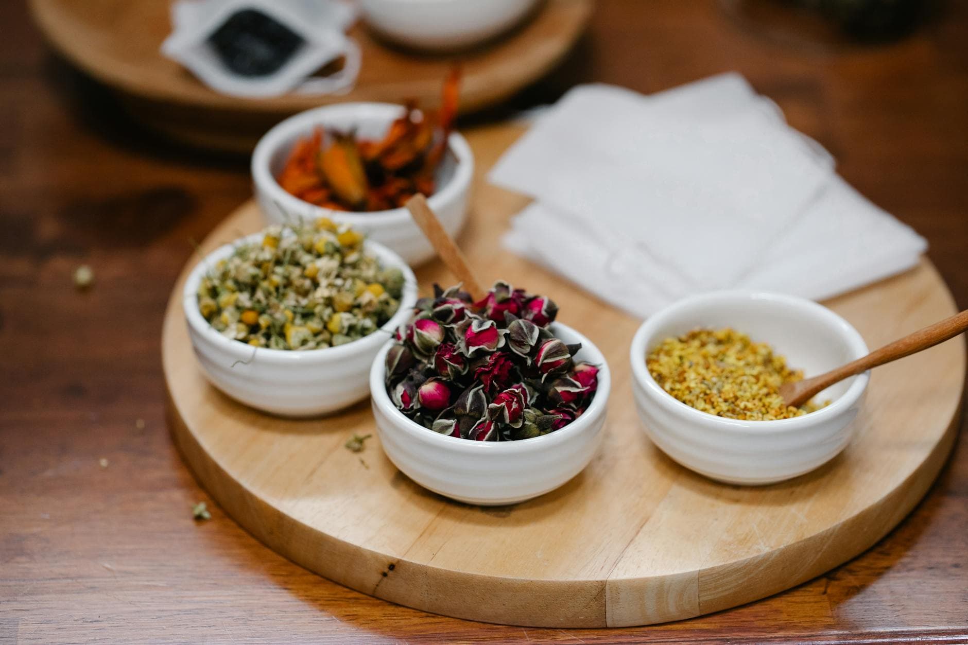 Various dried herbs and spices in white bowls on wooden tray, showing the ingredient range used in full production recipe development