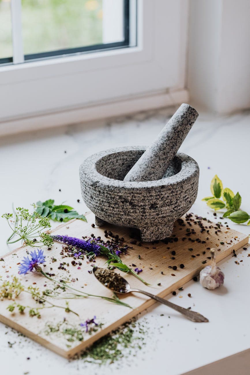 Stone mortar and pestle with scattered herbs and spices on wooden board