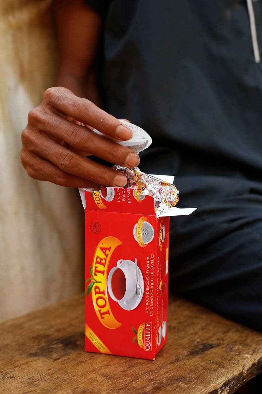 Person holding tea bag from open branded tea box - label information visible including origin, best-before date, and batch code