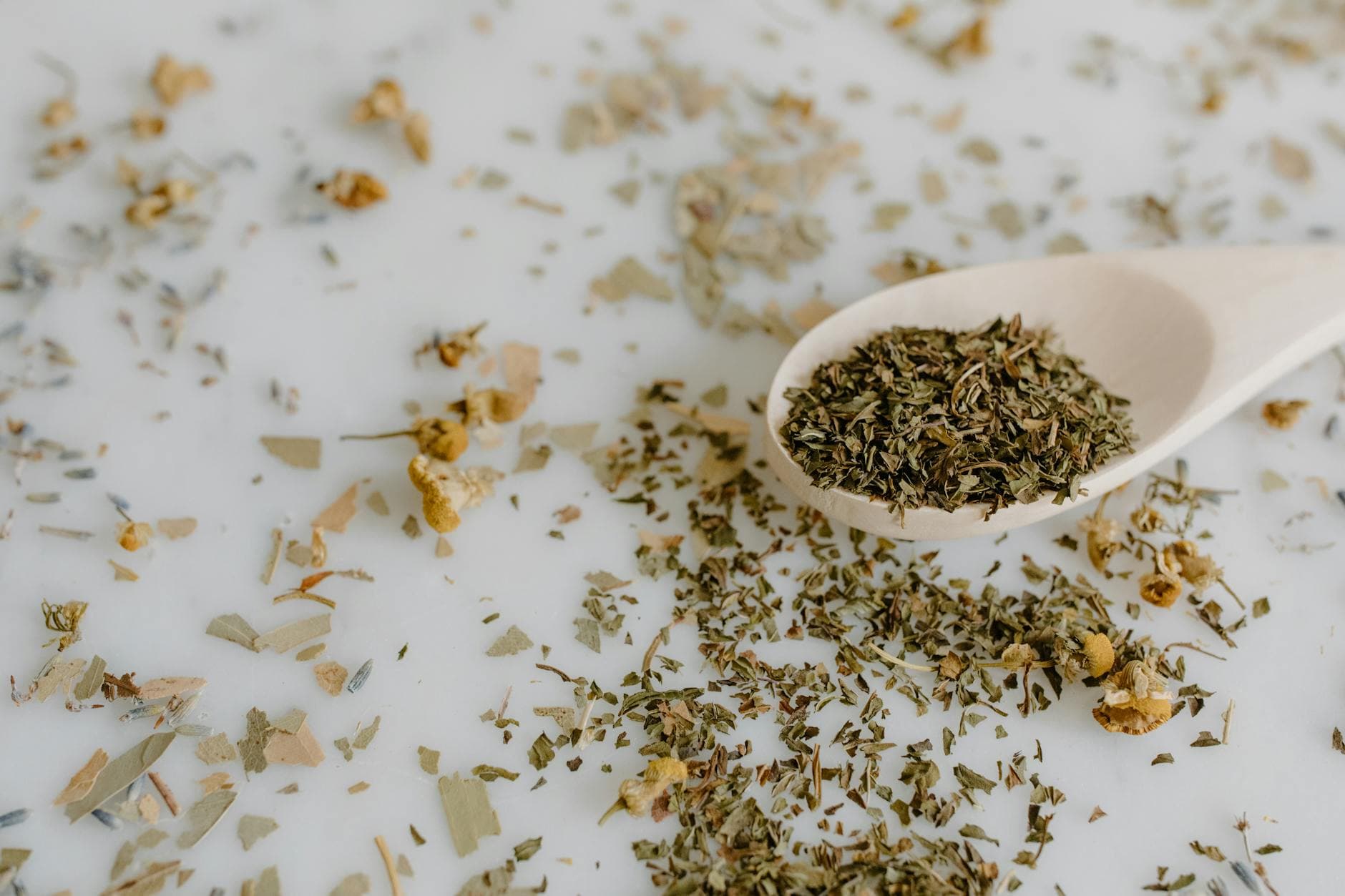 Close-up of dried herbs including thyme, sage and chamomile on a wooden spoon, showing natural texture and color