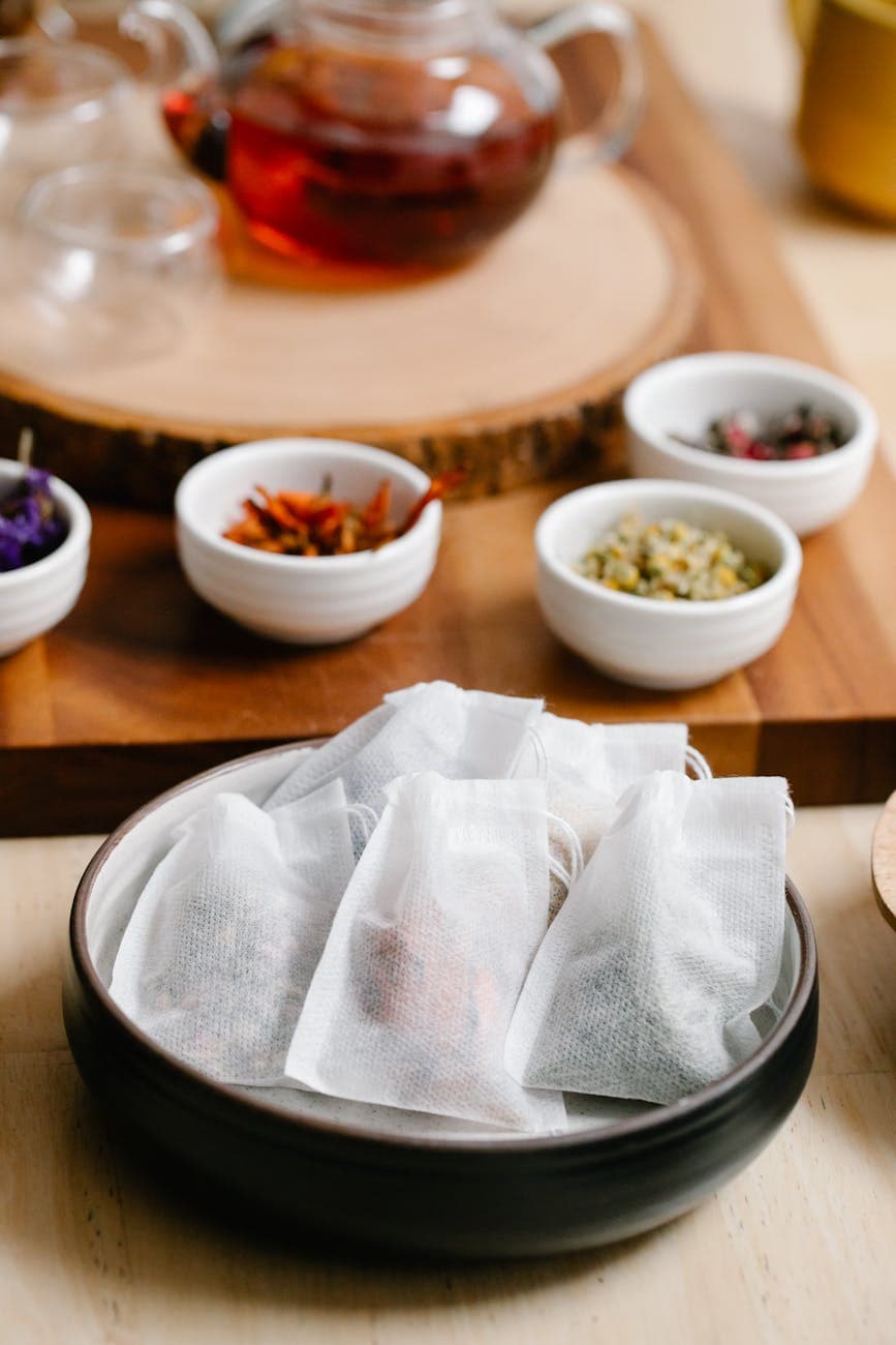 Herbal tea bags and bowls of dried herbs on a wooden table showing the natural ingredients used in tea bag production