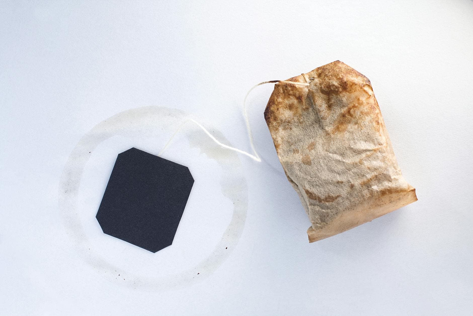 Close-up of a double-chamber paper tea bag and tag on a white surface, showing the double-knot string closure and cardboard tag