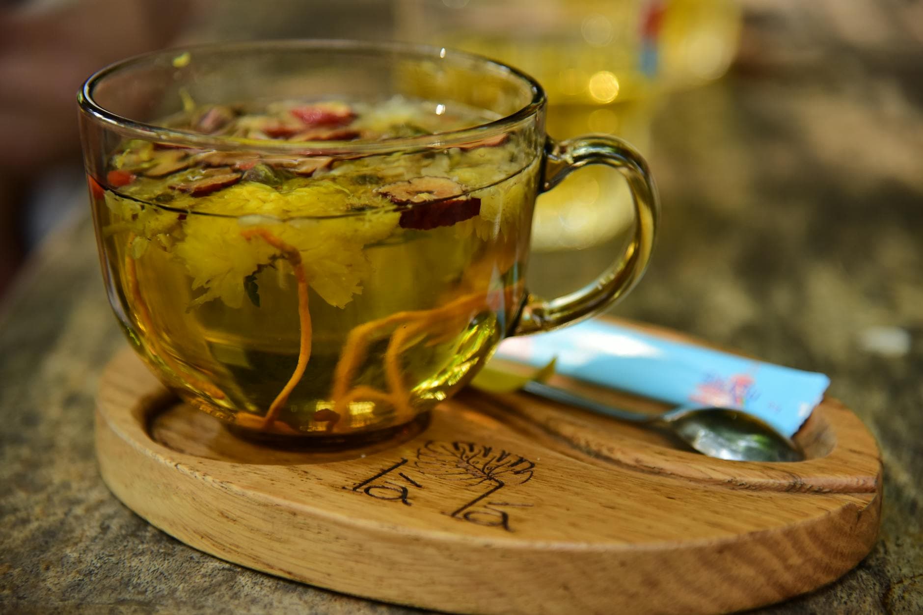Herbal tea brewing in a glass cup with dried flowers on a wooden tray - the finished product of the family herb supply chain since 1990.